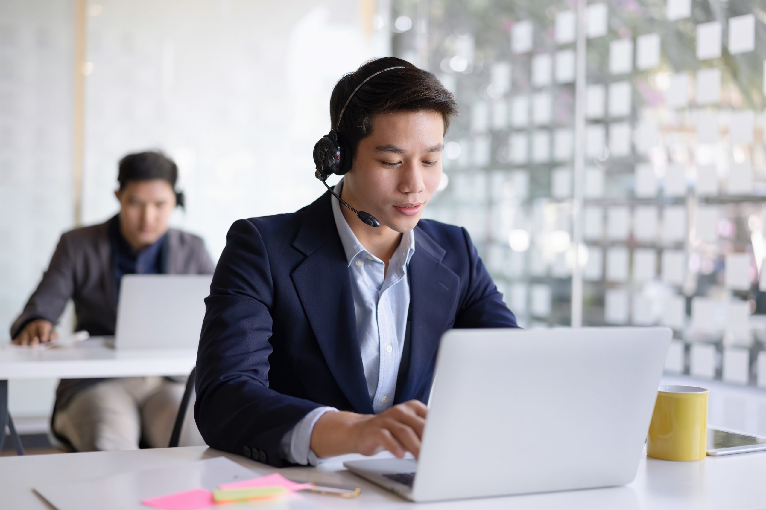 Attractive young asian male call center agent in headset consulting client
