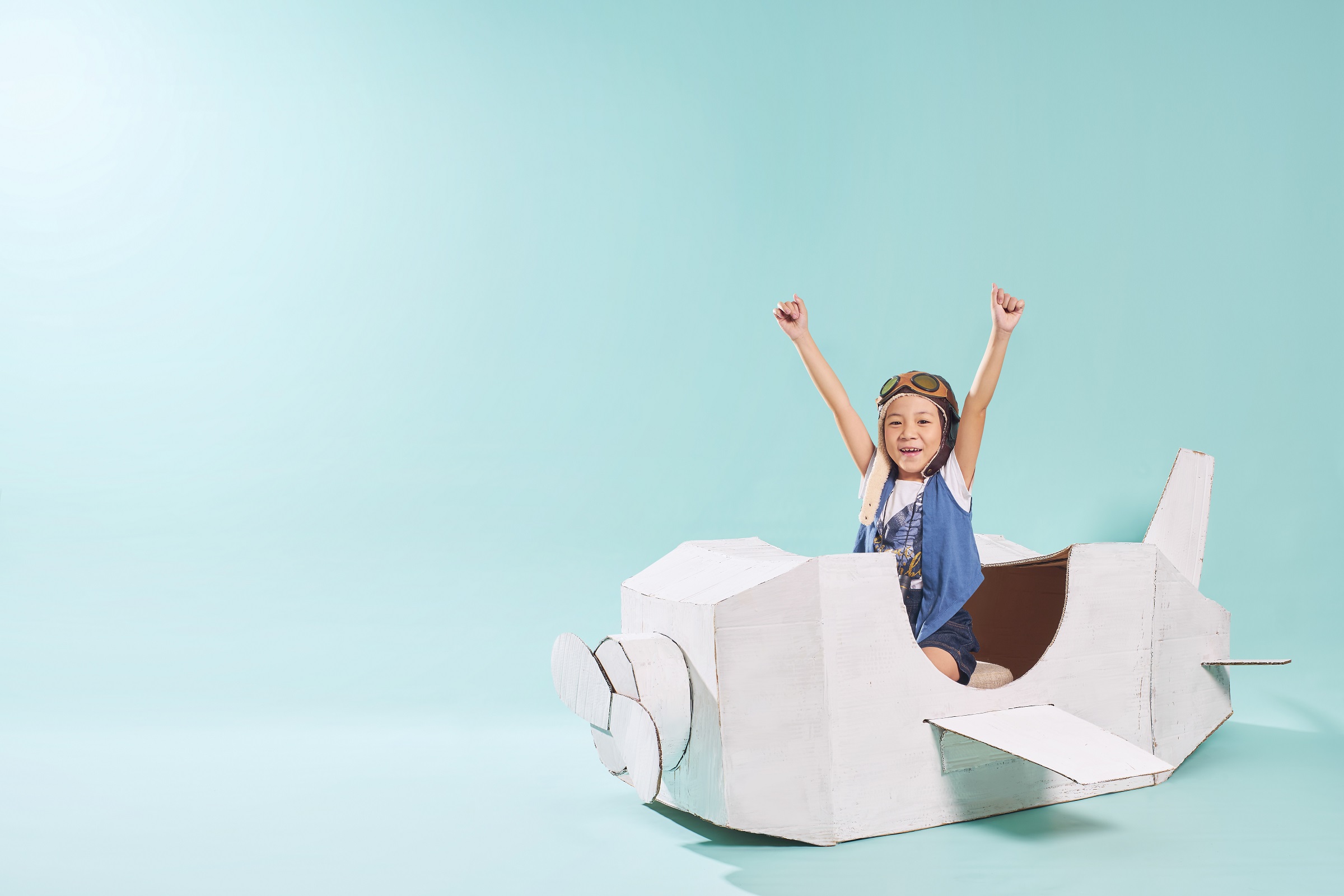 Little asian girl is happy sitting on a hand made cardboard paper plane . Isolated on mint green background
