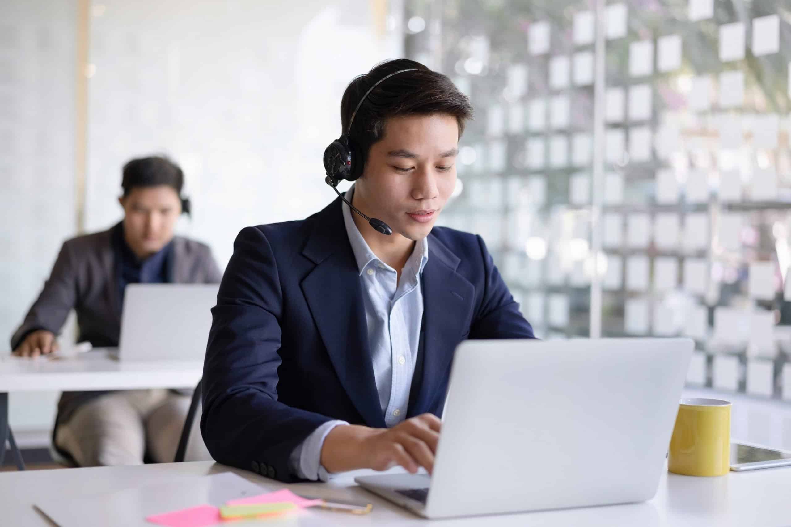 Attractive young asian male call center agent in headset consulting client