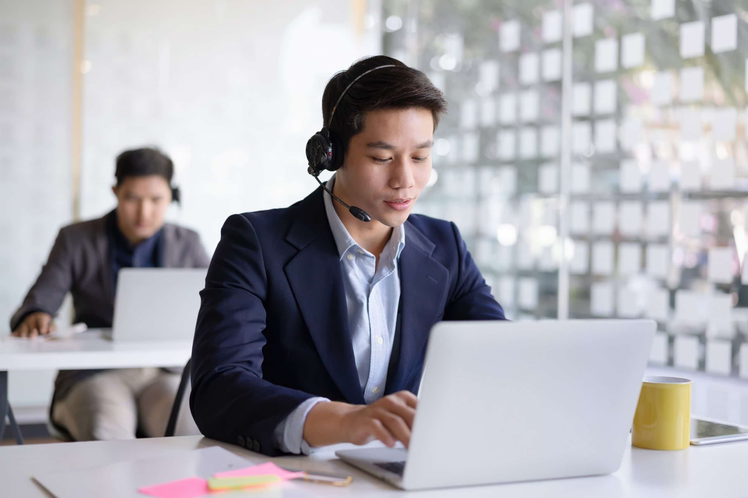 Attractive young asian male call center agent in headset consulting client