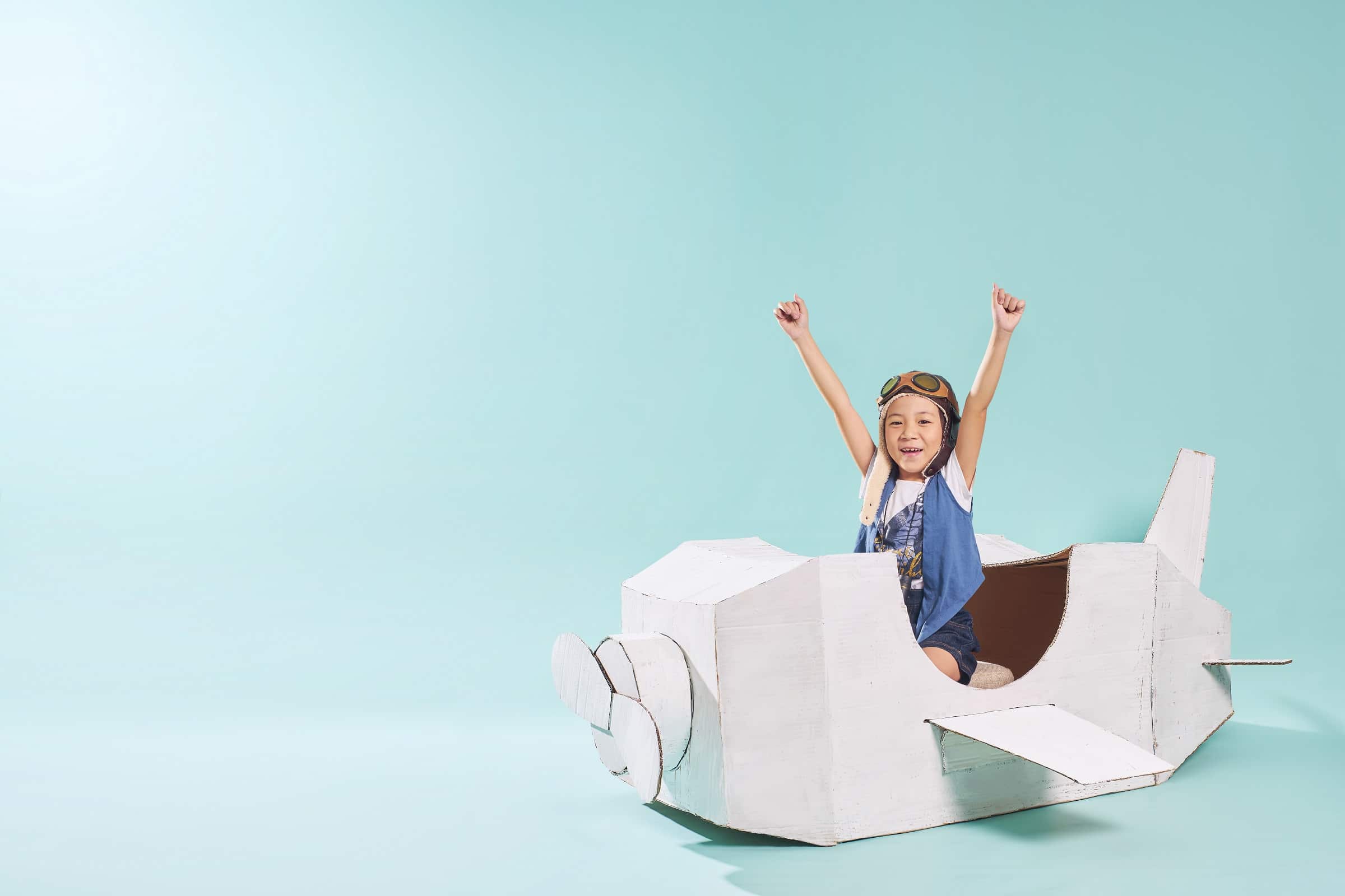 Little asian girl is happy sitting on a hand made cardboard paper plane . Isolated on mint green background